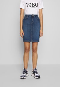 Jeanskjol i mörkblått, knälång, med framfickor och en figurnära design. Kombinerad med en vit grafisk T-shirt och sportiga sneakers.