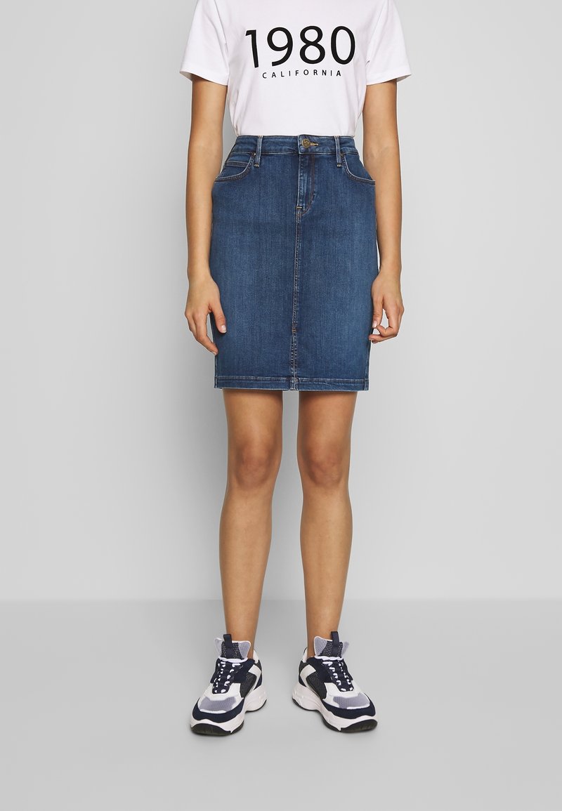 Jeanskjol i mörkblått, knälång, med framfickor och en figurnära design. Kombinerad med en vit grafisk T-shirt och sportiga sneakers.