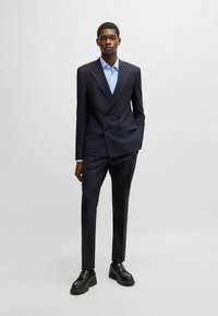 Abito doppiopetto blu navy realizzato in tessuto morbido, con un design aderente. Abbinato a una camicia a scacchi azzurro chiaro e scarpe nere chunky.