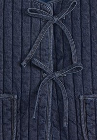 Gestepptes dunkelblaues Denim-Jackett mit Rundhalsausschnitt, doppelten Bindebändern und zwei aufgesetzten Vordertaschen mit kontrastierenden Nähten.
