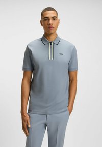 Jasnoszara koszulka polo z zamkiem przy kołnierzyku, z żó�łtymi i czarnymi paskami. Czarny logo "BOSS" na piersi. Gładka faktura.