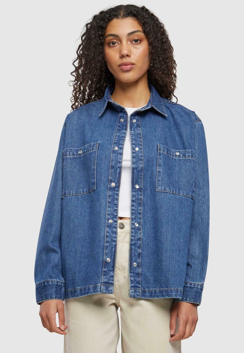 Blauw denim overhemd met twee borstzakken, knoopsluiting en lange mouwen, in een relaxte pasvorm met gestikte details langs de naden.