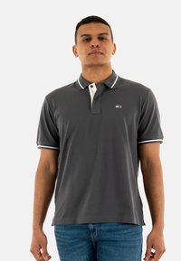 Camisa polo gris con cuello blanco y acentos a rayas; mangas cortas, confeccionada en una tela suave, con un pequeño logo en el pecho.