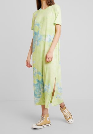 Femme portant une robe midi tie-dye vert clair et bleu avec manches courtes et fente latérale, associée à des baskets montantes beige