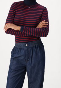 Haut à col roulé à rayures bleu marine et rouge à manches longues avec un petit logo, associé à un pantalon en denim foncé ample avec une taille élastique.