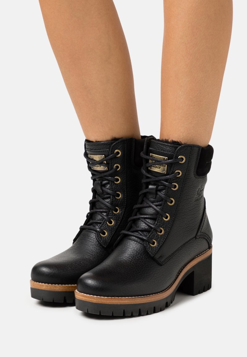 Bottes en cuir noir à finition texturée, œillets dorés et talon épais. Dotées d’un col doublé de fourrure et d’une semelle robuste pour une meilleure adhérence.