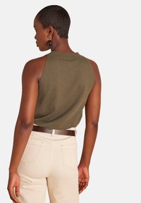 Top verde oliva senza maniche con scollo rotondo, abbinato a pantaloni beige chiaro a vita alta e cintura marrone, che presenta un design semplice.