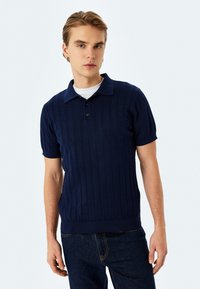 Marinblå kortärmad polo med ribbad textur, tre knappar och klassisk krage. Stylar med mörka denimjeans.