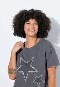 Grå oversized t-shirt lavet af bomuld. Har to stjernedesign med metalskruer. Korte ærmer og en bred halsudskæring.