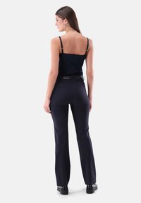 Marinefarbene Spaghettiträgertop, kombiniert mit enganliegenden, dunklen Hosen. Die Hosen haben eine glatte Textur und eine schlanke Silhouette, abgerundet mit einem eleganten Gürtel.