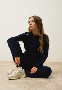 Pull en tricot côtelé marine et pantalon, associés à des baskets de course beige clair. Texture lisse, coupe décontractée et pantalon longueur cheville.