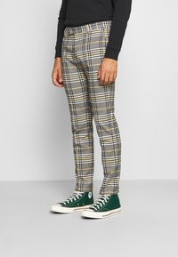 Kariérové kalhoty v šedé, žluté a černé barvě se slim fit střihem. Doplněné o zelené vysoké tenisky s bílými akcenty.