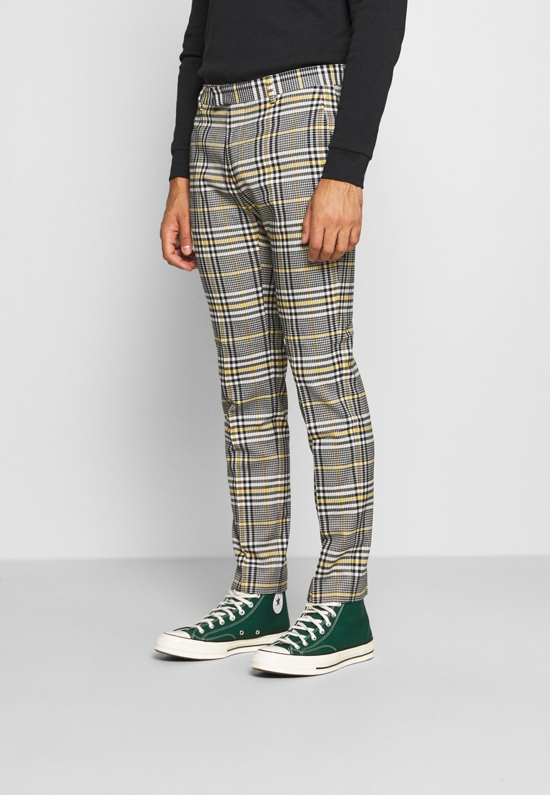 Kariérové kalhoty v šedé, žluté a černé barvě se slim fit střihem. Doplněné o zelené vysoké tenisky s bílými akcenty.