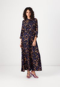 Long, flowy dress in dark blue fabric with a colorful abstract pattern of orange and blue shapes. Features a button-down front and collar.