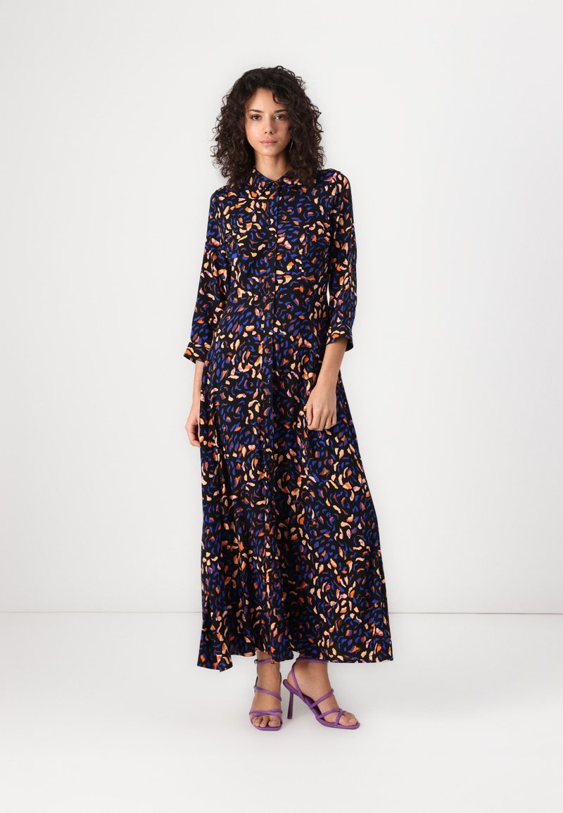 Long, flowy dress in dark blue fabric with a colorful abstract pattern of orange and blue shapes. Features a button-down front and collar.