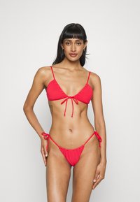 Piros bikini szett, texturált háromszög alakú toppal, állítható pántokkal és illeszkedő, alacsony derekú alsóval, amelyek együtt formálják az alakot.