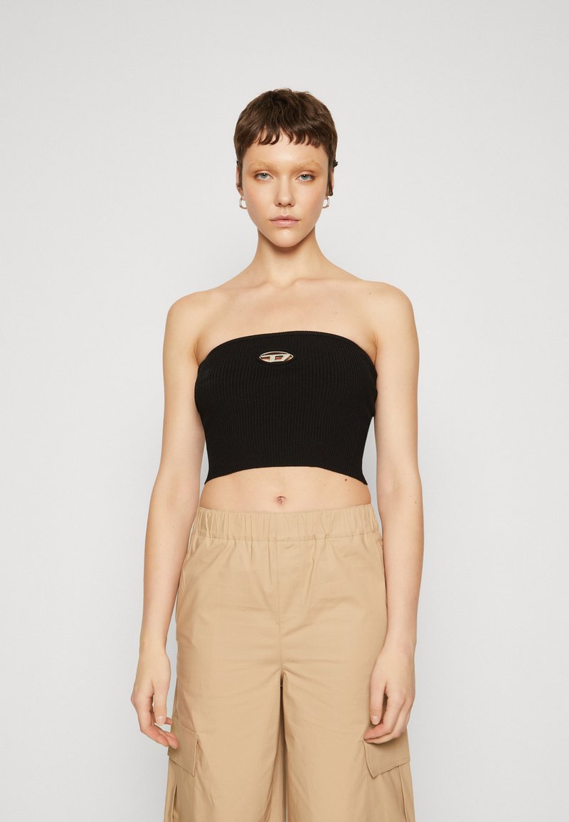 Černý žebrovaný strapless crop top s kovovým logem umístěným uprostřed. Modelka zkombinovala s béžovými cargo kalhotami. Jednoduchý, přiléhavý design.