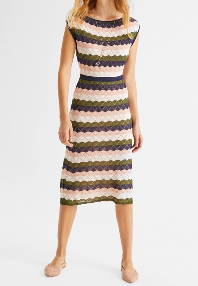 Femme portant une robe sans manches longueur genou avec des rayures horizontales festonnées en rose, vert olive, bleu marine et blanc, associée à des ballerines couleur nude.