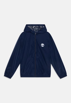 Chaqueta cortavientos con capucha azul marina, cremallera completa en el frente, puños elásticos y logotipo blanco de árbol en el área del bolsillo izquierdo del pecho.
