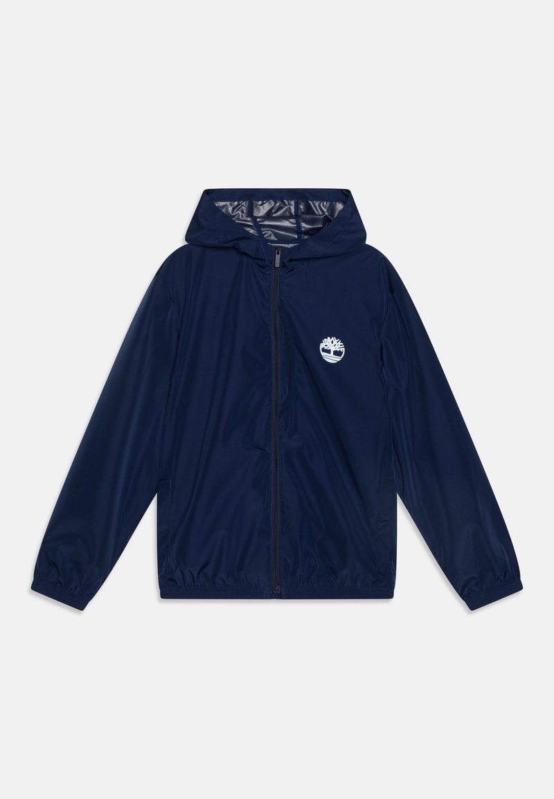 Blouson coupe-vent à capuche bleu marine avec fermeture éclair intégrale à l'avant, poignets élastiques et logo d'arbre blanc sur la zone de la poche poitrine gauche.