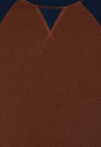 Brun bomulls-T-shirt med design av ärmar i marinblå raglanstil, med V-ringning och kontrasterande sömsyning vid axlarna.