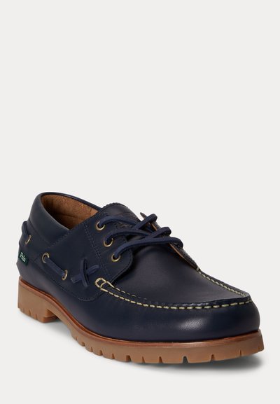 Granatowy skórzany but typu boat z jasnobrązową gumową podeszwą, sznurowanym przodem, kontrastującymi szwami oraz zieloną tkaninową metką Polo po boku.