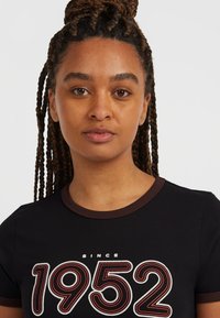 Svart bomull t-shirt med rund halsringning och brunt kantband samt en iögonfallande grafik "1952". Korta ärmar och en åtsittande silhuett.