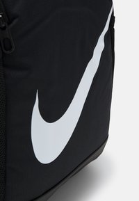Svart ryggsäck i strukturerad tyg med en stor vit Nike-logga. Har dragkedja och meshnätsfickor.