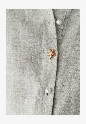 Lniana koszula w jasnoszarym kolorze o teksturowanym wykończeniu, z perłowymi guzikami i akcentem w postaci złotej rozgwiazdy w pobliżu górnego guzika.