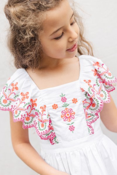 Λευκό βαμβακερό φόρεμα με πολύχρωμη κεντητική με λουλούδια σε ροζ, πορτοκαλί και πράσινο, με βολάν στα μανίκια και εφαρμοστό μπούστο.