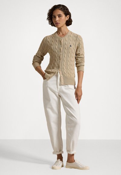 Cardigan en tricot beige à boutons sur le devant, associé à un pantalon ample de couleur crème et des baskets claires. Design simple et coupe décontractée.