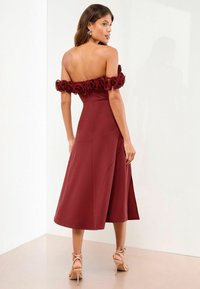 Burgundy midi-mekko, jossa on olkaimeton röyhelöyksityiskohta, vartalonmyötäinen yläosa ja levenevä helma, yhdistettynä nuden värisiin sandaaleihin.