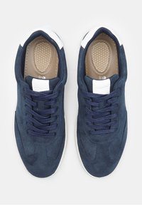 Tumedas sametist tennisetossud valgete aktsentidega, ümar varvas, siledad paelad ja tekstuuriga sissevaatamine. Sile pind kontrastsete servadega.