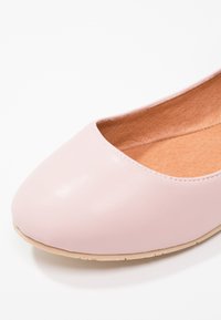 Chaussure plate de ballet en cuir rose clair avec bout arrondi et semelle beige sur fond blanc.
