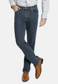 Jeans de mezclilla azul oscuro con un diseño de pierna recta, que cuentan con cinco bolsillos y sutiles detalles de costura, combinados con zapatos de vestir marrones claros.