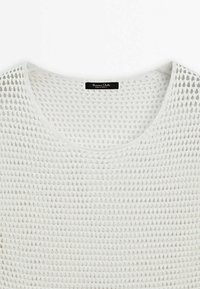 Vitt stickat tröja med ett löst, öppet nätmönster. Har en bred rund halsringning och en enkel etikett på baksidan.