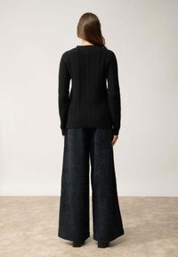 Czarny prążkowany sweter z długimi rękawami, w połączeniu z szerokimi, teksturowanymi ciemnymi spodniami oraz botkami na słupku. Widok z tyłu.