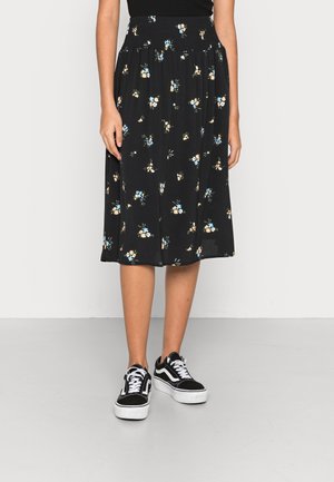Zwarte midirok met kleine blauwe en beige bloemenprint, gecombineerd met zwart-witte sneakers en een zwart topje.