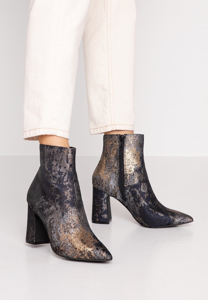 Bottines en matériau noir et doré à motif, avec un bout pointu et un talon block haut. Dotées d'une fermeture éclair sur le côté.