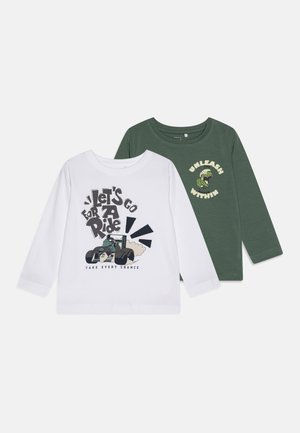 Zwei Langarm-T-Shirts; eines weiß mit einem Traktor-Graphic und Text, das andere dunkelgrün mit einem Dinosaurier-Graphic und Text. Baumwollstoff, runde Ausschnitte.