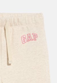 Μπεζ βαμβακερές φόρμες με ελαστική μέση, κορδόνι και το λογότυπο "GAP" με ροζ περίγραμμα στην περιοχή της τσέπης.