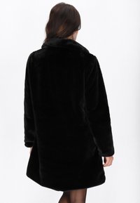 Palton din blană sintetică neagră, cu guler, mâneci lungi și o croială lejeră, având o textură moale și un design până la genunchi.