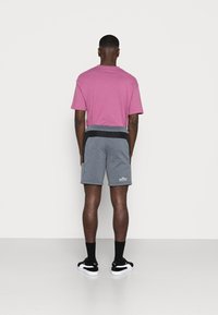 Růžové tričko s krátkým rukávem v kombinaci s šedými sportovními šortkami, které mají černý pas a kapsy. Černé ponožky a černé boty dotvářejí vzhled.