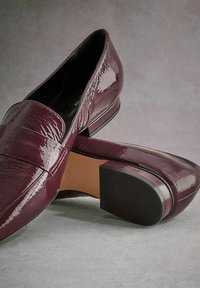 Burgundy patent leather loafers with a low block heel, featuring a smooth texture, wide band across the front, and a solid black outsole.