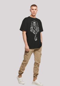 Black T-shirt with a skull and octopus design in gray, paired with beige cargo pants. White sneakers complete the casual look.