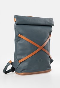 Zaino in pelle blu scuro con spallacci in pelle marrone. Chiusura a rullo e superficie testurizzata. Presenta un logo sul lato.