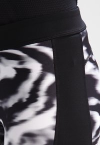 Zwart-witte sport leggings met een breed zwarte tailleband, een gladde stoftextuur en een contrasterend zijpaneelontwerp.