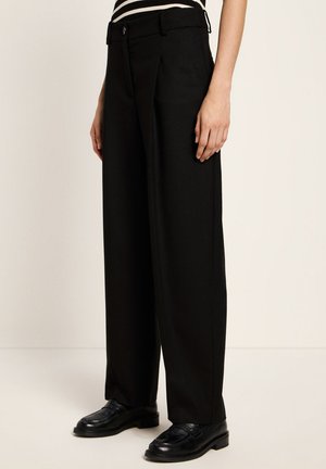 Black wide-leg trousers with a high waist, featuring a front pleat, sleek fabric, and a single button closure. Paired with glossy black shoes.