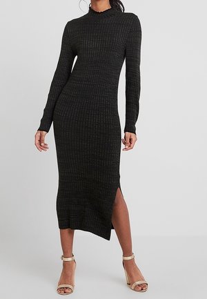 Vestido negro de punto acanalado con cuello alto, mangas largas y abertura lateral. Presenta una silueta ajustada y tejido texturizado.