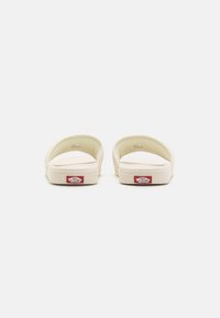 Vans slip-on cipele, boje kreme, od gumene tkanine, otvorenog dizajna straga, ravna potplat, s crvenim logotipom na peti. Glatka tekstura.